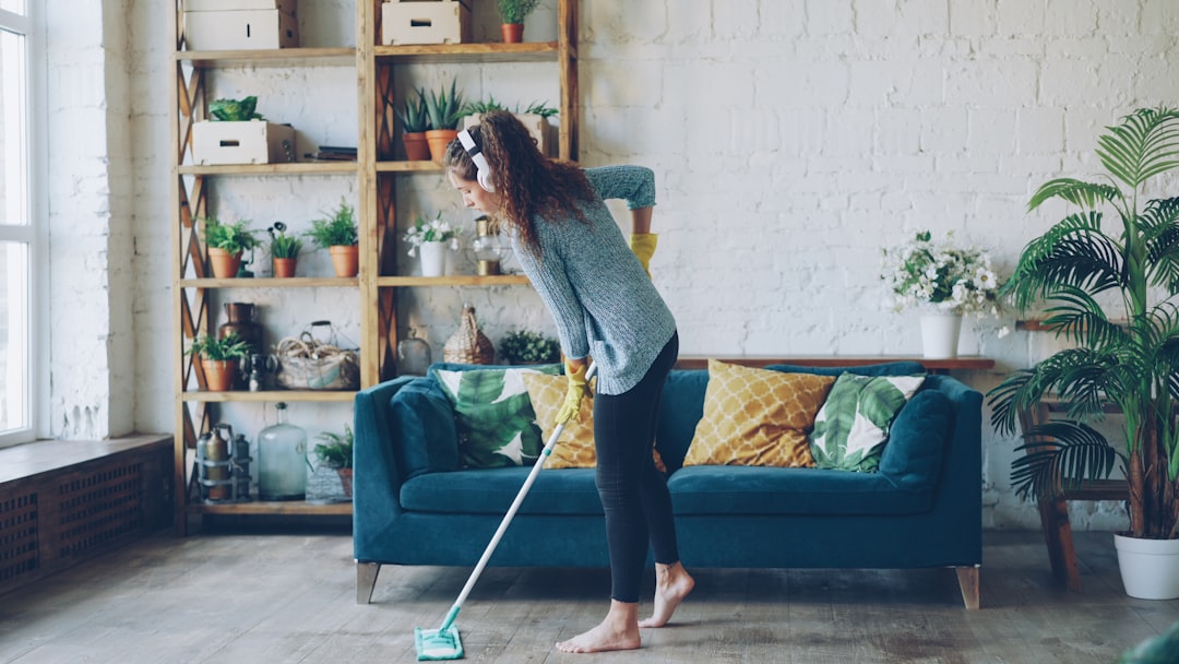 Pretty girl with dark curly hair wearing casual clothing is mopping floor at home and listening to music through headphones. Clean-up, modern houses and people concept.