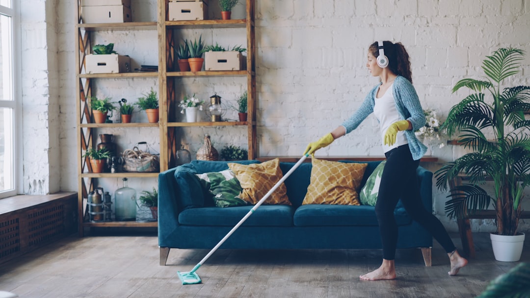 services-01 Cheerful young woman is dancing with mop during routine clean-up in nice loft style apartment, she is listening to music with wireless headphones and singing enjoying her occupation.